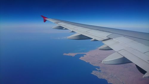 Airplane wing over an island landscape against blue sky