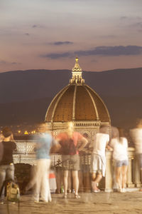 People at illuminated temple against sky during sunset