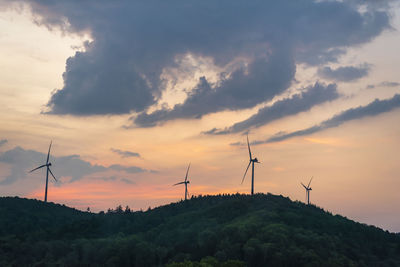 Low angle view of wind turbines on mountain against cloudy sky during sunset