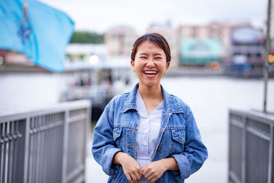 Portrait of happy young woman standing against river