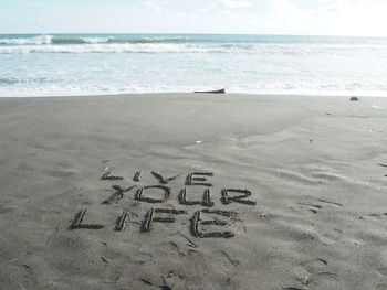 Close-up of text on sand at beach against sky