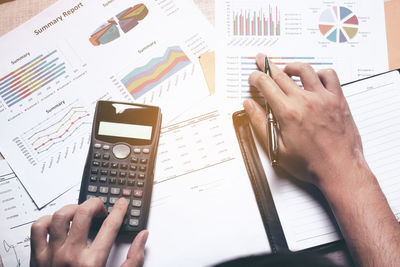 Close-up of businessman working over graph while using calculator on table 