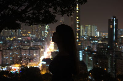 Woman standing against illuminated city at night