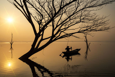 Silhouette bare tree by lake against sky during sunset