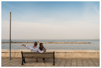 Rear view of couple sitting at beach against sky