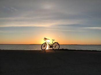 Bicycle by sea against sky during sunset