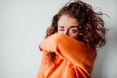 Portrait of woman covering face with hand against wall