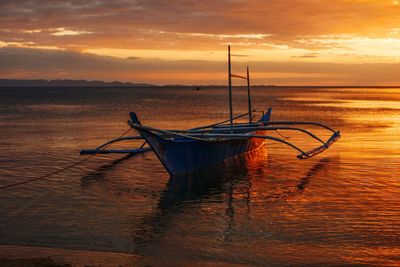 Fishing boat moored in sea against sky during sunset