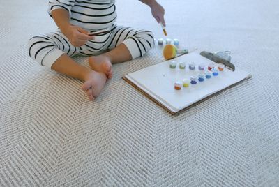 Low section of boy with watercolor paints sitting on carpet at home