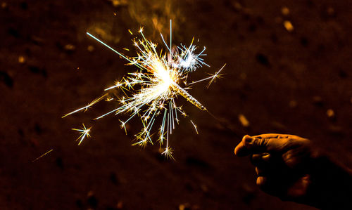 Cropped hand of person holding illuminated sparkler at night