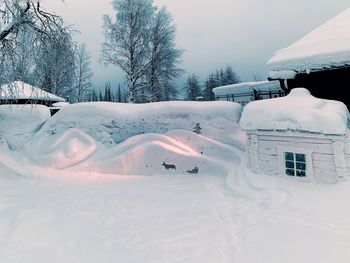 Snow covered field by building against sky
