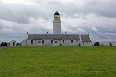 Lighthouse on field by building against sky