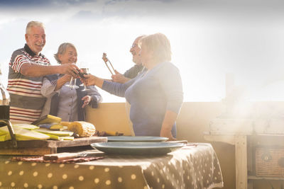 Cheerful senior friends toasting drinks at balcony during party
