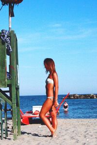Side view of woman wearing bikini at beach against blue sky