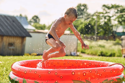 Boy jumps in the pool in the summer on the lawn, drops of spray in the sun.