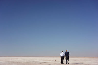 Men walking on salt flat against clear sky