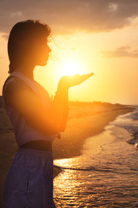 Silhouette of a young caucasian woman holding the sun in her hands. on the seashore at sunset.