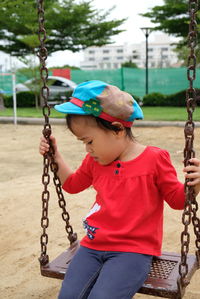 Cute girl looking away while sitting on swing in playground