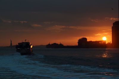 Silhouette built structures in calm sea at sunset