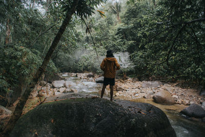 Rear view of man standing by rocks in forest