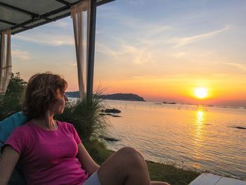 Side view of woman looking at sea against sky during sunset