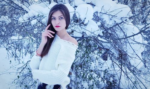 Portrait of young woman standing against snow covered plants