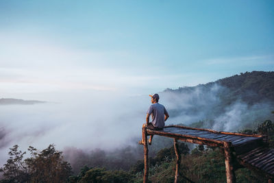 Rear view of man standing on mountain against sky