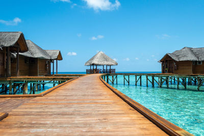 Pier amidst houses by sea against blue sky