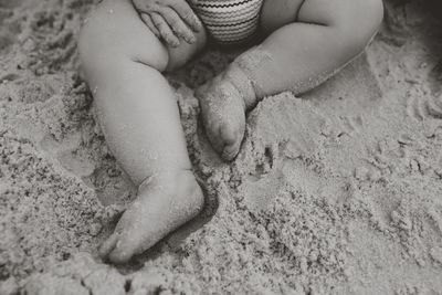 Low section of baby girl sitting on sand at beach