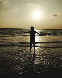 Silhouette man standing on beach against sky during sunset