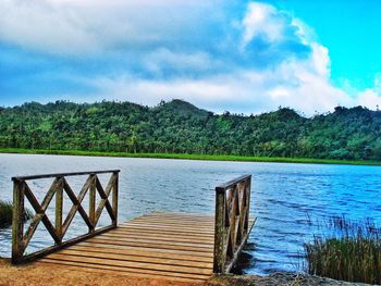 Wooden pier on lake against cloudy sky