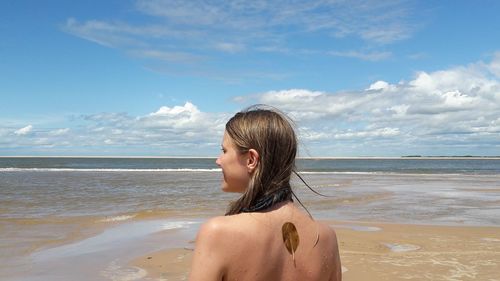 Rear view of shirtless woman standing at beach against sky