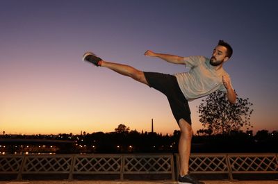 Full length of young man kicking against sky during sunset