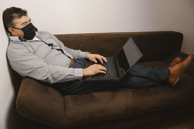 High angle view of man using laptop sitting on sofa at home