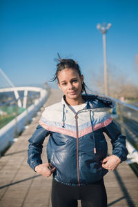 Young woman in jacket standing on footbridge against sky