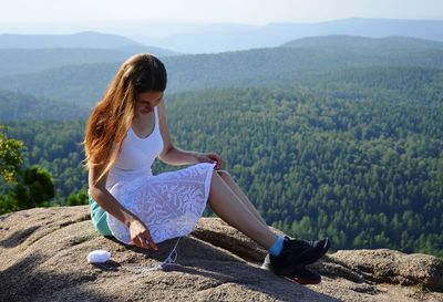 Young woman crocheting while sitting on rock against trees