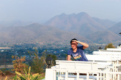 Man shielding eyes while standing against mountains