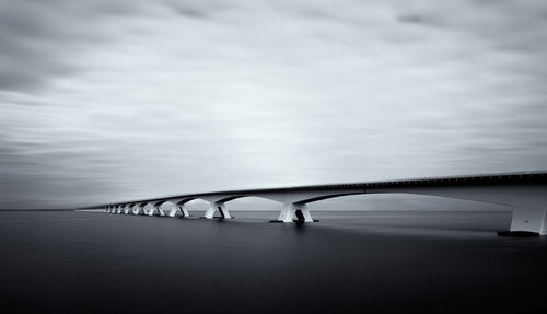 Bridge over river against cloudy sky