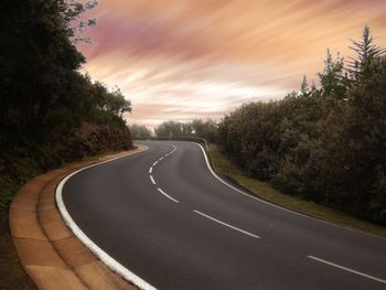 Empty road amidst trees against sky during sunset