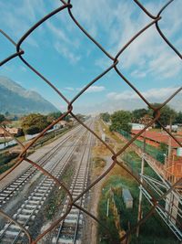 Railroad tracks against sky seen through chainlink fence