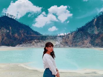 Portrait of young woman standing at beach against sky