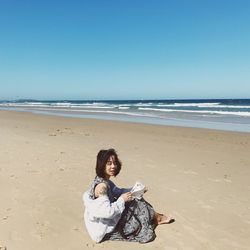 Full length of woman sitting at beach against sky