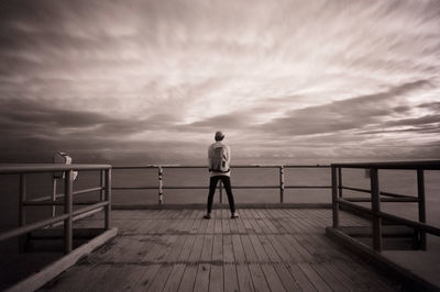 Rear view of man standing by railing against sky