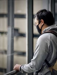 Side view of young man looking away through floor length windows.