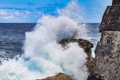 Waves splashing on rocks against sky