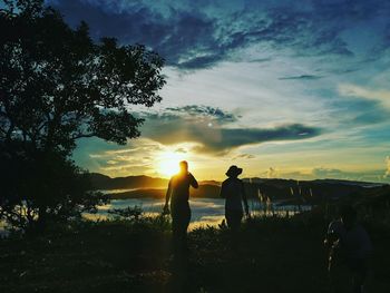 Rear view of silhouette people standing on field against sky during sunset