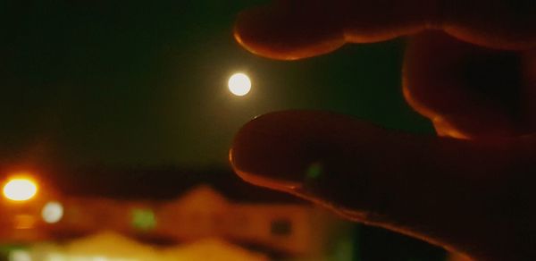 Close-up of hand holding illuminated lights against sky at night