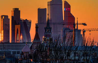 Spasskaya tower and skyscrapers in city against clear sky during sunset