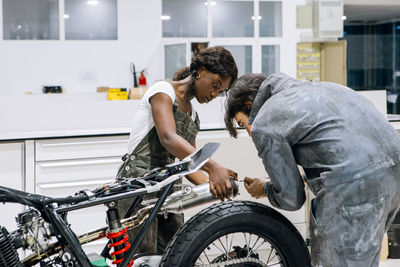 Side view of diverse technicians in workwear repairing muffler of custom motorbike while working together in bright workshop