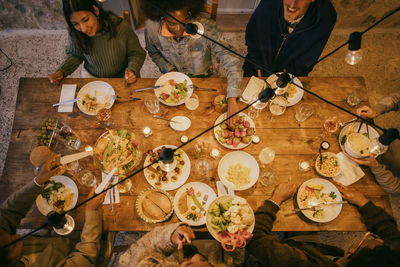 High angle view of multiracial friends sitting at illuminated dining table during dinner party